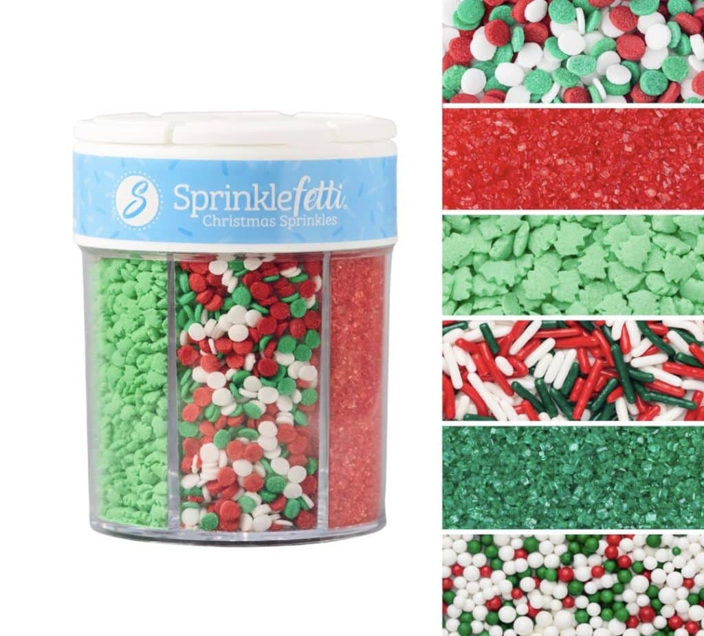 A container of Sprinklefetti Christmas Sprinkles is perfect for decorating Snow Globe Cookies, featuring six festive varieties: red sugar, green chips, red sanding sugar, holiday nonpareils, green sugar, and Christmas jimmies. Each section offers a unique texture and color combination.